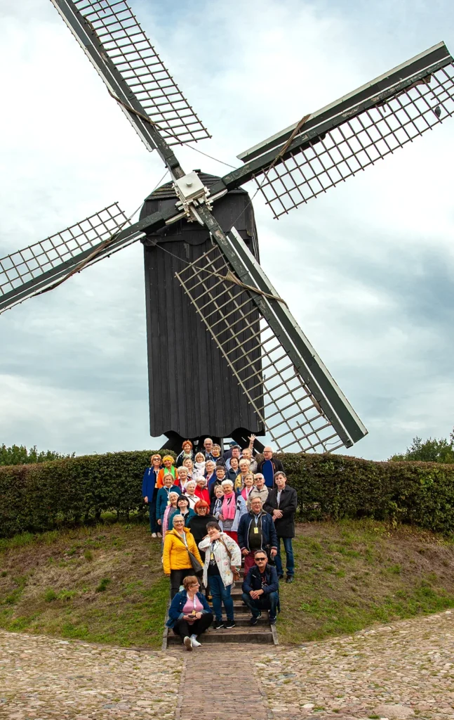 Zdjęcie przedstawiające grupę seniorów przed wielkim wiatrakiem